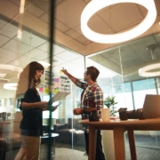 Zwei junge Geschäftsleute arbeiten zusammen in einem Büro und stehen vor einer Glaswand mit Post Its.
